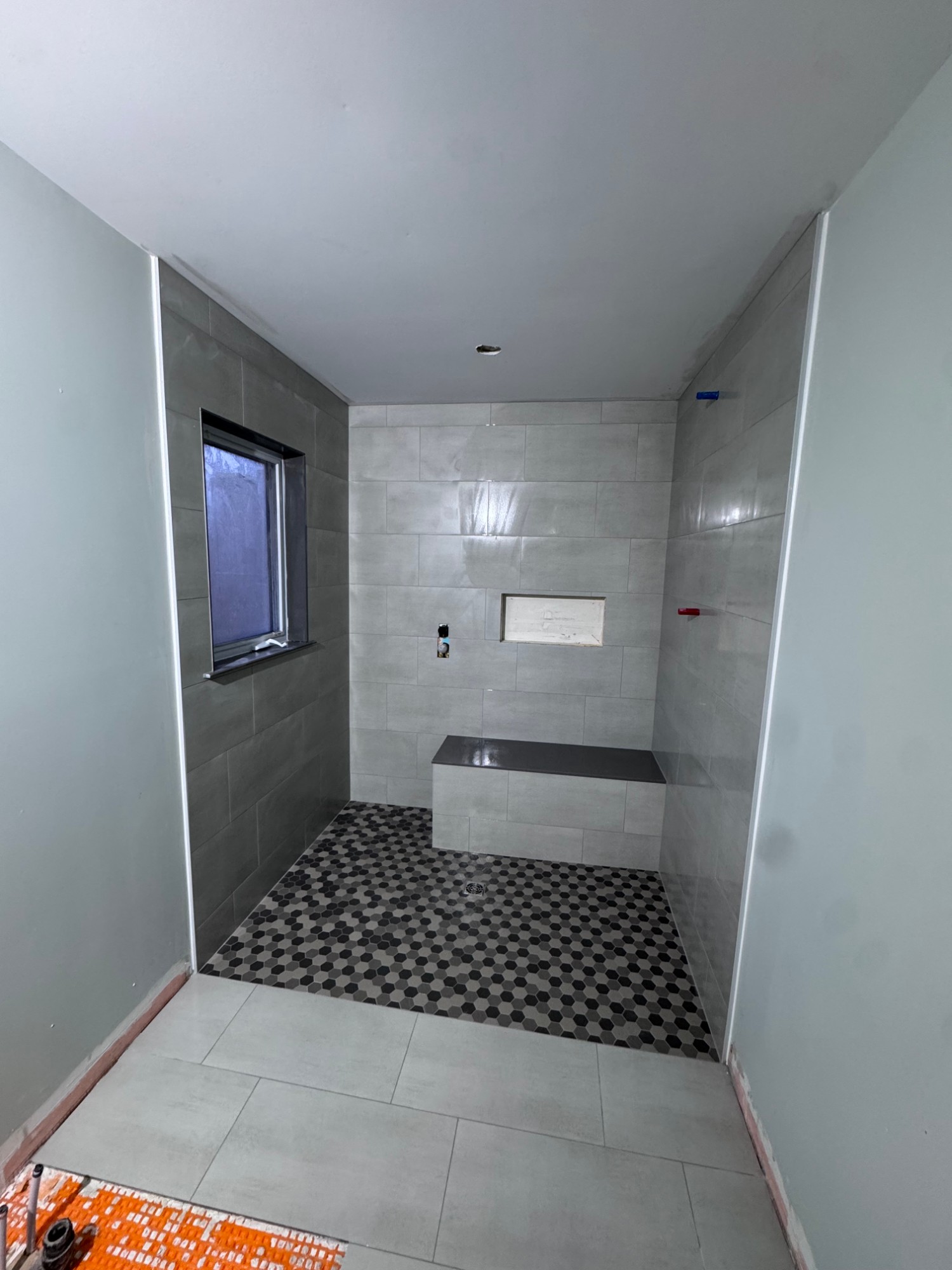 Large walk-in shower with grey tile walls, hexagon mosaic floor and built-in bench