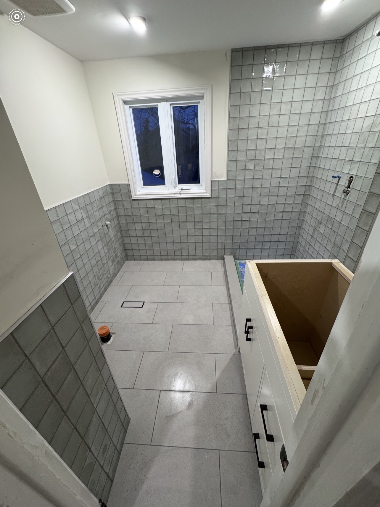 Bathroom under construction with grey square tile walls and white large-format floor