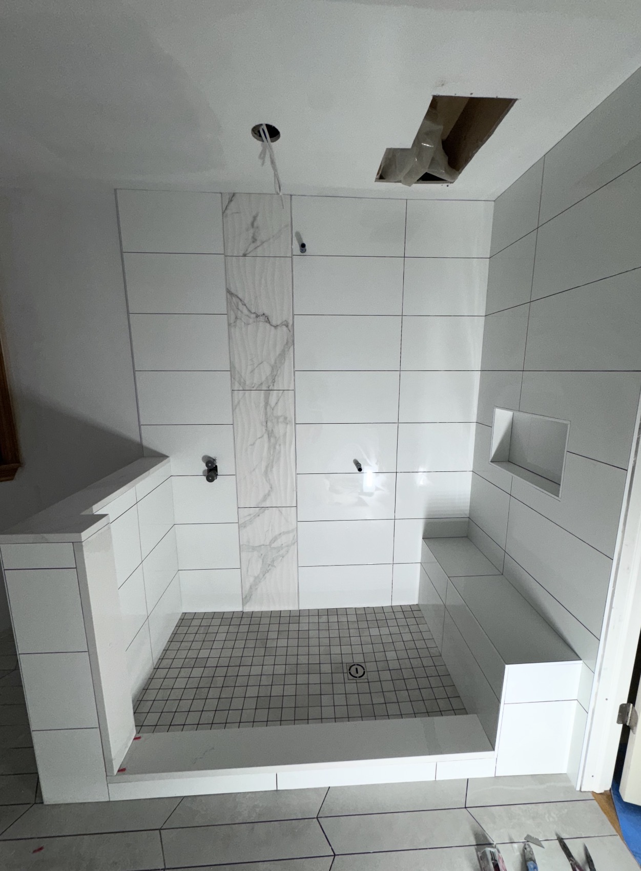 Walk-in shower with white tile walls, marble accent strip, built-in bench and niche